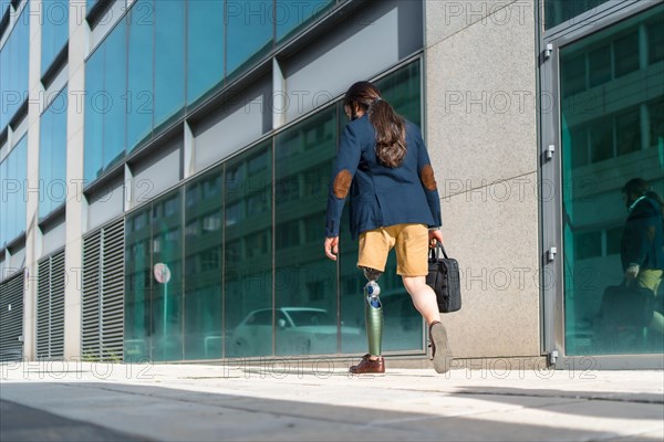 Rear view photo with copy space of a businessman with amputee leg walking along a financial district street