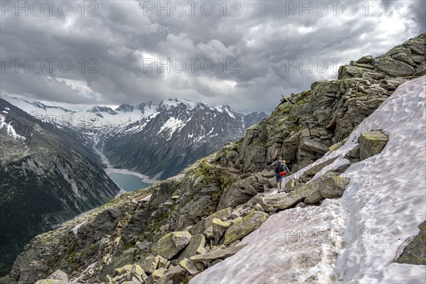 Mountaineer on hiking trail with snow, view of Schlegeisspeicher, glaciated rocky mountain peaks Hoher Weisszint and Hochfeiler with glacier Schlegeiskees, Berliner Hoehenweg, Zillertal Alps, Tyrol, Austria, Europe