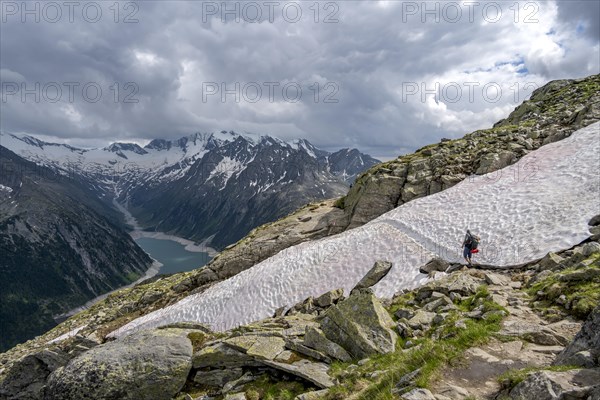 Mountaineer on hiking trail with snow, view of Schlegeisspeicher, glaciated rocky mountain peaks Hoher Weisszint and Hochfeiler with glacier Schlegeiskees, Berliner Hoehenweg, Zillertal Alps, Tyrol, Austria, Europe