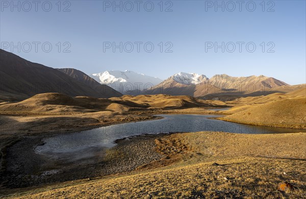 White glaciated and snowy mountain peak Pik Lenin at sunrise, mountains reflected in a lake between golden hills, Trans Alay Mountains, Pamir Mountains, Osh Province, Kyrgyzstan, Asia