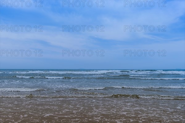 Rough ocean waves and white caps under a blue sky with low wispy cirrus clouds