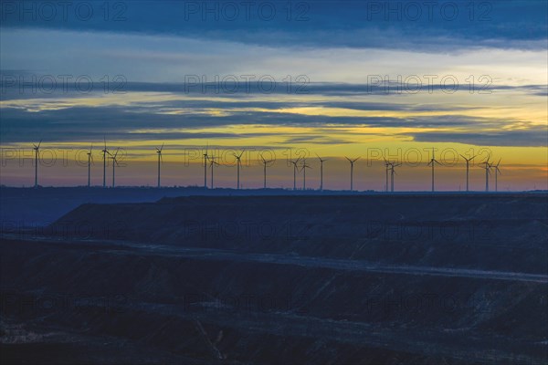 Row of wind turbines on the horizon under a colourful evening sky, open-cast lignite mine, North Rhine-Westphalia, Germany, Europe