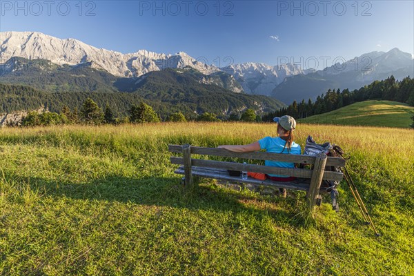 Hiker sitting on a bench in front of mountains, woman, summer, afternoon, Eckbauer, Garmisch-Partenkirchen, Wetterstein range, Bavaria, Germany, Europe