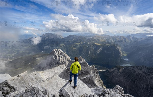 Mountaineer on the rocky summit of the Watzmann Mittelspitze, Watzmann crossing, view of mountain panorama with Steinernes Meer and Koenigssee, Kleiner Watzmann and Watzmann children, Berchtesgaden National Park, Berchtesgaden Alps, Bavaria, Germany, Europe
