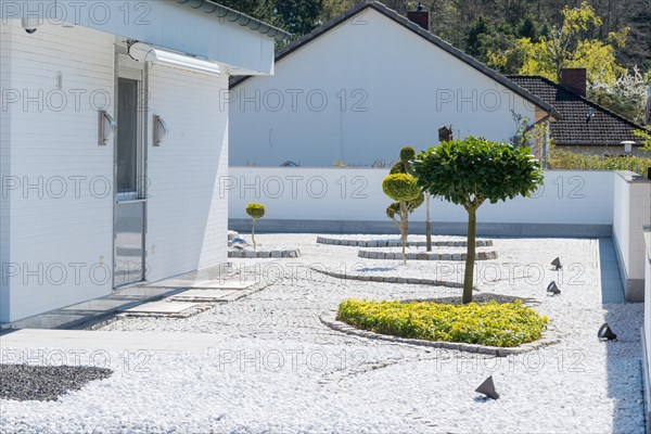 Modern garden with geometric shapes and spotlights next to a white house, residential design in bright colours, orderly garden with artfully trimmed trees and paved paths, gravel garden with white walls, garden hostile to nature and animals with trimmed plants, contrary to regulations, violation of building regulations, sealing, gravel desert, non-ecological garden design, Lower Saxony, Germany, Europe