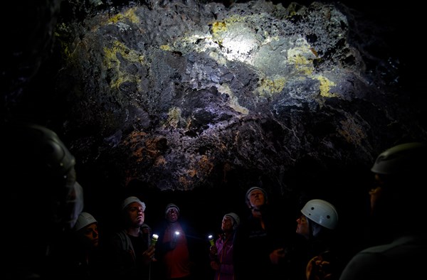 A group of people in helmets listen to a guide in the lava tunnel Gruta das Torres, Gruta das Torres, Pico, Sao Miguel, Faial, Azores, Portugal, Europe