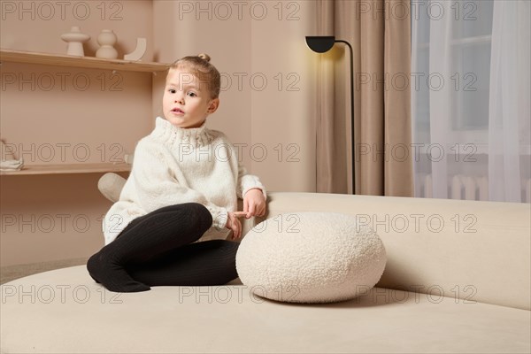 Cute little girl sits on sofa, watching to the side and listening to someone