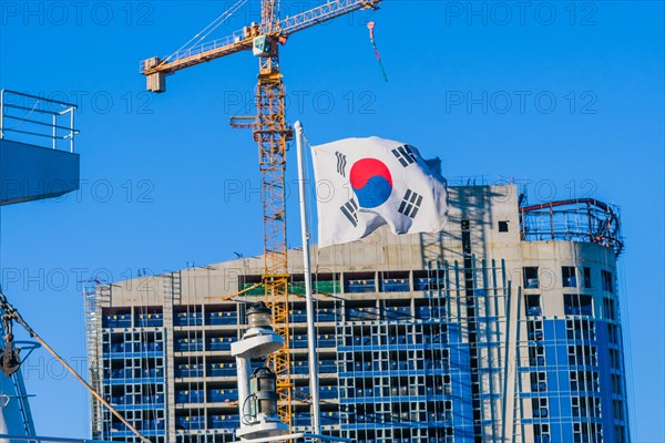 Korean flag on flying from a ship in front of a construction crane attached to a building under construction