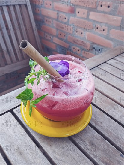 Vertical view of a refreshing watermelon juice with a bamboo straw and an edible flower, healthy vegan summer drink