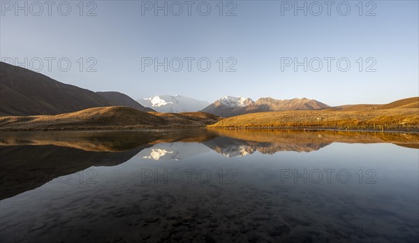 White glaciated and snowy mountain peak Pik Lenin at sunrise, mountains reflected in a lake between golden hills, Trans Alay Mountains, Pamir Mountains, Osh Province, Kyrgyzstan, Asia