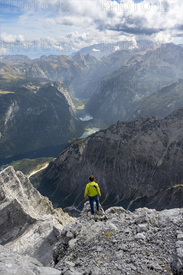 Mountaineer on the rocky summit of the Watzmann Mittelspitze, Watzmann crossing, view of mountain panorama with Steinernes Meer and Koenigssee, Berchtesgaden National Park, Berchtesgaden Alps, Bavaria, Germany, Europe