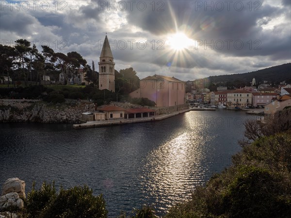 Morning sun breaking through clouds, view of the harbour entrance of Veli Losinj, with St. Anthony's Church, island of Losinj, Kvarner Gulf Bay, Adriatic Sea, Croatia, Europe