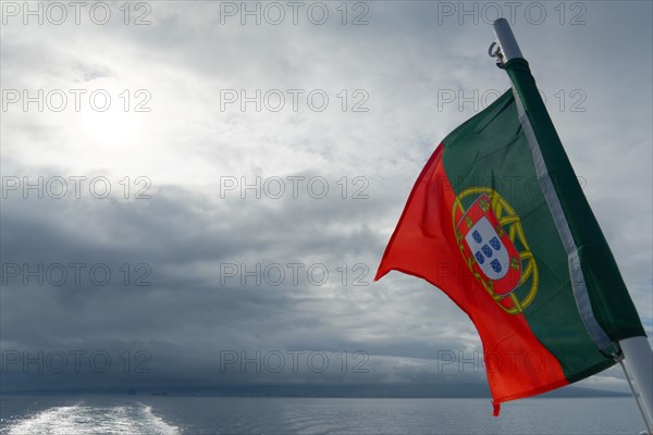 Portuguese flag waving majestically against a cloudy sky over the sea, Horta, Faial Island, Azores, Portugal, Europe
