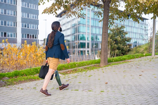 Rear view of a businessman with prosthetic leg walking along an urban park