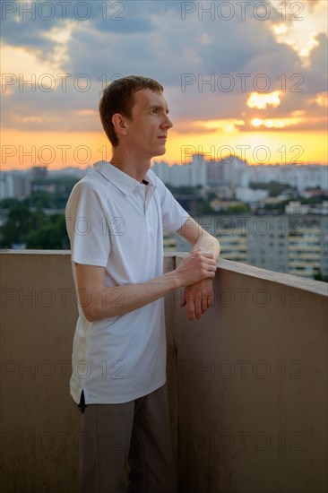 Man in white polo shirt standing on balcony in dusk