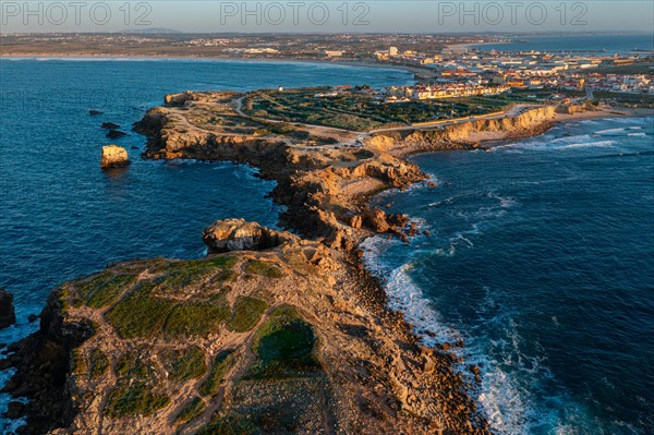 Aerial landscape of Peniche, Portugal, peninsula and town at sunset. Summer sunset haze, little foliage and rocky cliffs, peninsula and rocks, fishing town, horizon, Europe