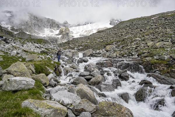 Mountaineers at a mountain stream, behind them rocky mountains with glacier Furtschaglkees, Furtschaglhaus, Berliner Hoehenweg, Zillertal, Tyrol, Austria, Europe