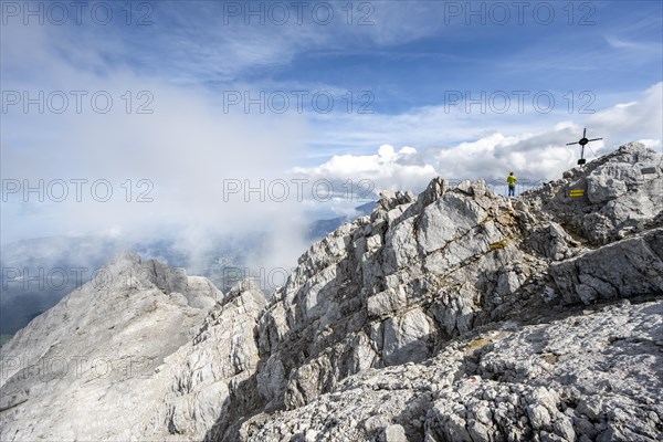 Mountaineer on the rocky summit of the Watzmann Mittelspitze with summit cross, Watzmann crossing, Berchtesgaden National Park, Berchtesgaden Alps, Bavaria, Germany, Europe