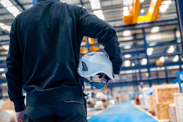 Rear view of an unrecognizable worker holding a helmet in a factory