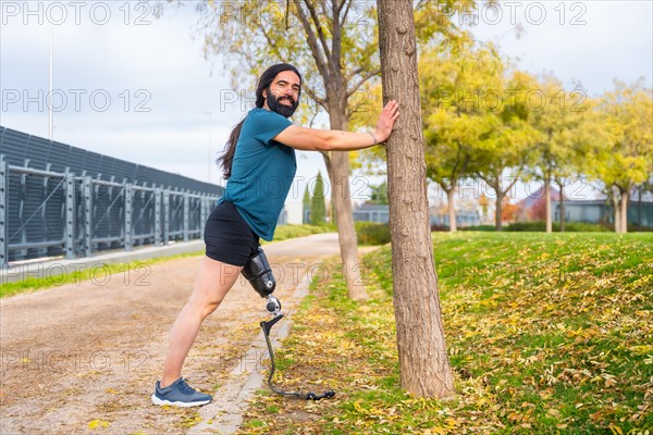 Happy disabled man with prostethic leg stretching in a park after running