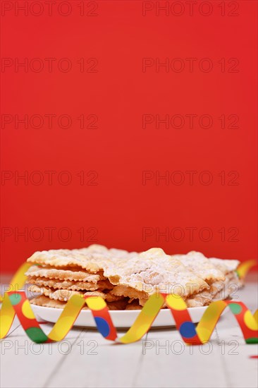 Fried Italian dessert snack for carnival season called 'Galani', ' Chiacchiere' or 'Crostoli' in front of red background. Also known as Angel Wings pastry