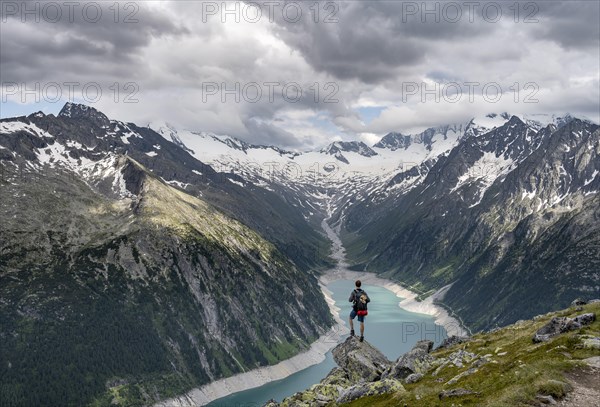 Mountaineer on a rock in front of a mountain panorama, view of Schlegeisspeicher, glaciated rocky mountain peaks Hoher Weisszint and Hochfeiler with glacier Schlegeiskees, Berliner Hoehenweg, Zillertal Alps, Tyrol, Austria, Europe