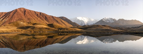 White glaciated and snowy mountain peak Pik Lenin at sunset, mountains reflected in a lake between golden hills, Trans Alay Mountains, Pamir Mountains, Osh Province, Kyrgyzstan, Asia