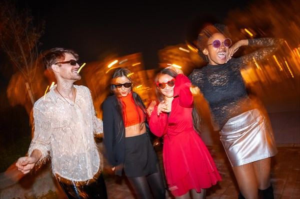 Night photo with flash and motion of four stylish friends dancing in the street