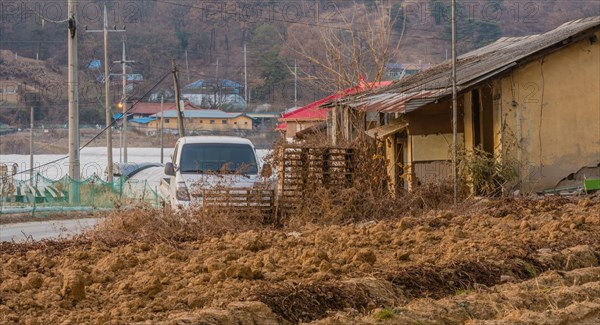 White truck parked next to an old run down abandoned shack with red roof house and small community in rural setting