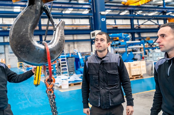 Three male engineers of a logistic factory using an industrial crane