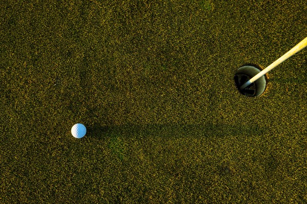 Golf Ball on the Grass with Shadow and Hole with Flag Pole on Putting Green on Golf Course in Sunset in Switzerland