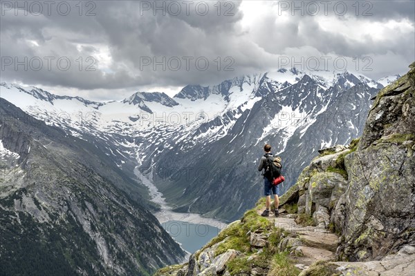 Mountaineer on hiking trail, view of Schlegeisspeicher, glaciated rocky mountain peaks Hoher Weisszint and Hochfeiler with glacier Schlegeiskees, Berliner Hoehenweg, Zillertal Alps, Tyrol, Austria, Europe