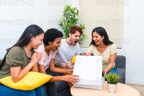 Happy multiracial friends sitting on a couch opening pizza box to eat at home