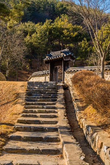 Stone steps leading to oriental gate with ceramic tile roof at mountainous woodland public park