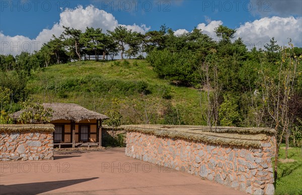 Old thatch roof building behind mud and stone wall at urban public park