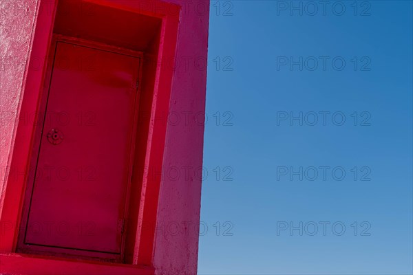 Closeup of door on red lighthouse with blue sky in background