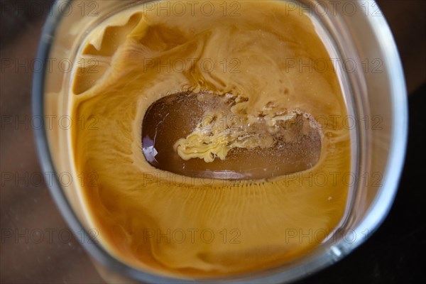 A close-up of an iced coffee with a melting ice cube creating ripples