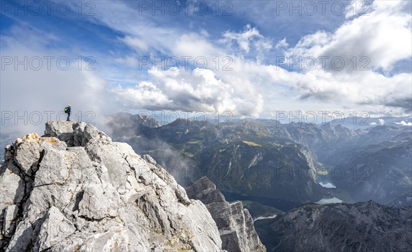 Mountaineer on the rocky summit of the Watzmann Mittelspitze, Watzmann crossing, view of mountain panorama with Steinernes Meer and Koenigssee, Berchtesgaden National Park, Berchtesgaden Alps, Bavaria, Germany, Europe