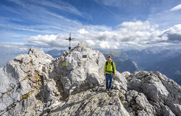 Mountaineer on the rocky summit of the Watzmann Mittelspitze with summit cross, Berchtesgaden National Park, Berchtesgaden Alps, Bavaria, Germany, Europe