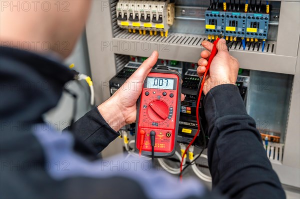 Worker measuring and repairing an electrical system panel in a factory