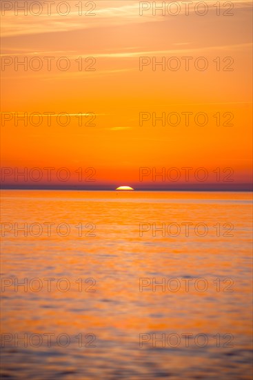 Intense, atmospheric sunset with bright orange-yellow sky over the Baltic Sea, only a small part of the sun disc still visible above the sea horizon, calm water, Hiddensee Island, Mecklenburg-Western Pomerania, Germany, Europe