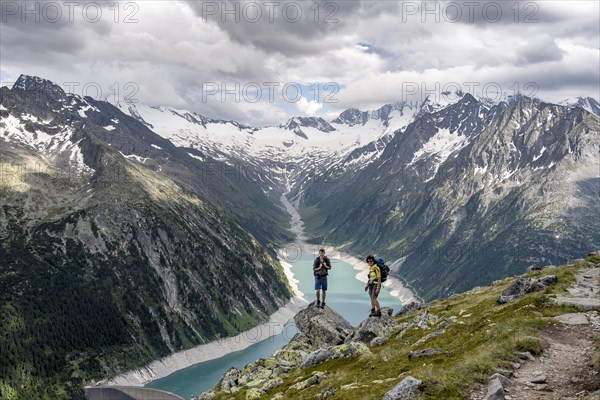 Two mountaineers on a rock in front of a mountain panorama, view of Schlegeisspeicher, glaciated rocky mountain peaks Hoher Weisszint and Hochfeiler with glacier Schlegeiskees, Berliner Hoehenweg, Zillertal Alps, Tyrol, Austria, Europe
