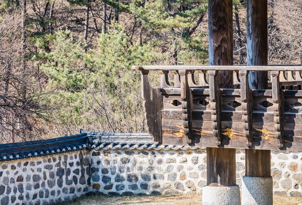 Wooden gazebo on concrete pillars surrounded by a stone wall in a local woodland park in South Korea