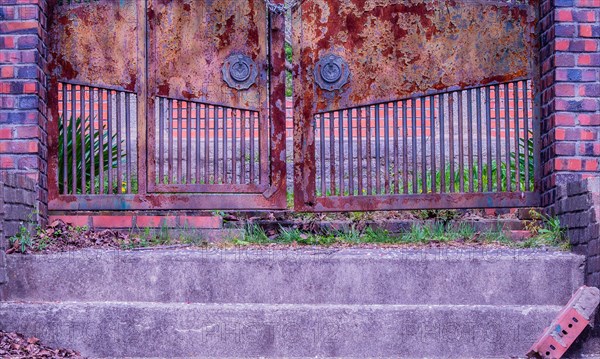 View of stairs leading to a chained rusted gate with red brick columns on each side located at old abandoned picnic pavilion in woodland area in South Korea