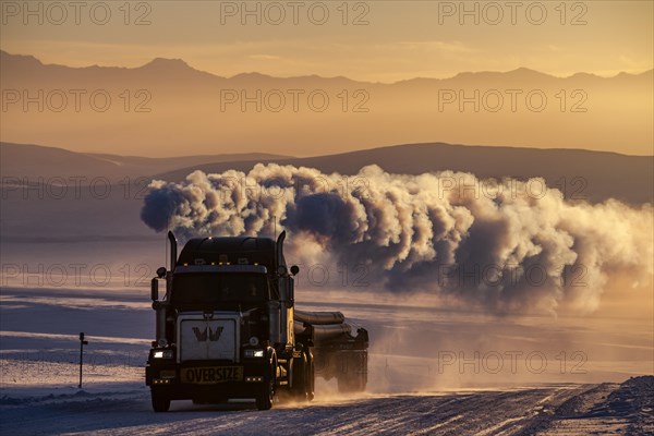 Truck on snowy track with large exhaust cloud in front of mountains in winter, evening light, Dalton Highway, Alaska