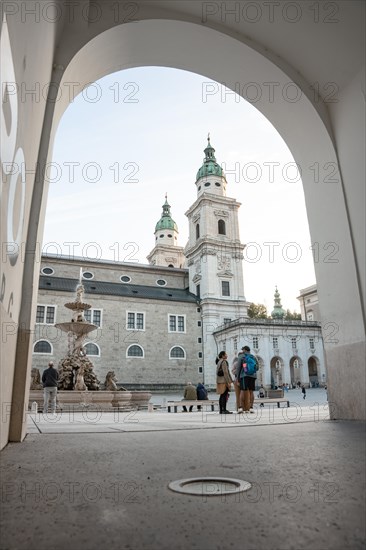 View of a square with people through an arch with a church in the background, Salzburg, Austria, Europe