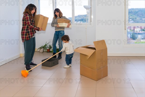A little girl plays with a broom while her mothers move into a new house