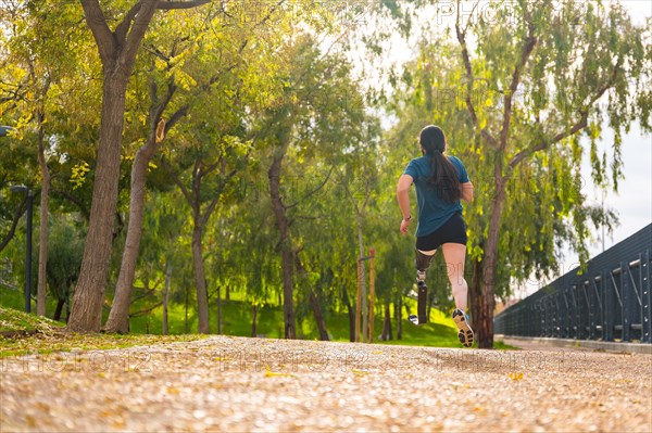 Rear view of an athlete with prosthetic leg running along a park