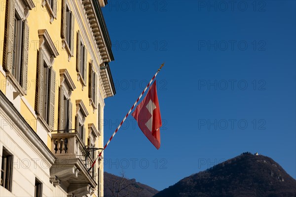 Swiss Flag on City Hall and Mountain Peak Monte Bre Against Blue Clear Sky in a Sunny Day in Lugano, Ticino, Switzerland, Europe