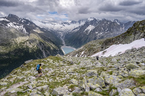 Two mountaineers on hiking trail, view of Schlegeisspeicher, glaciated rocky mountain peaks Hoher Weisszint and Hochfeiler with glacier Schlegeiskees, Berliner Hoehenweg, Zillertal Alps, Tyrol, Austria, Europe